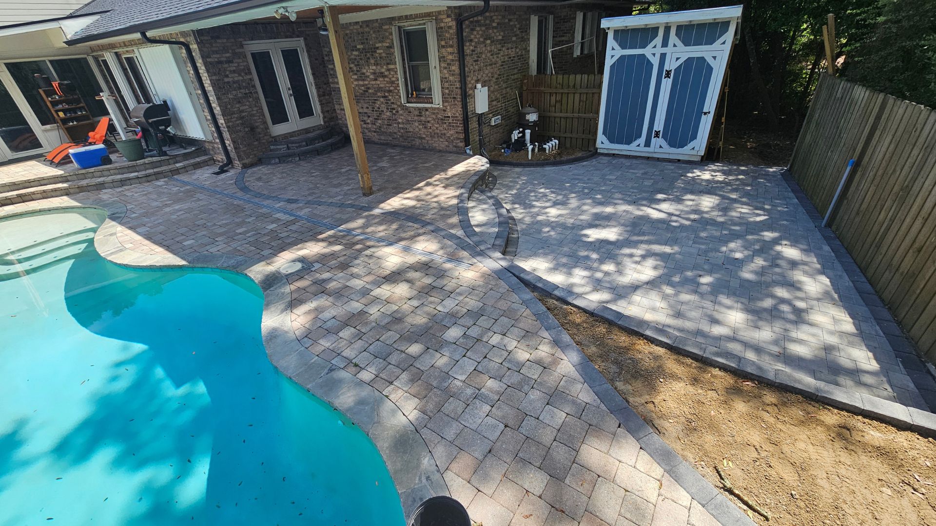 Backyard with blue pool, paver patio, brick house, and wooden shed