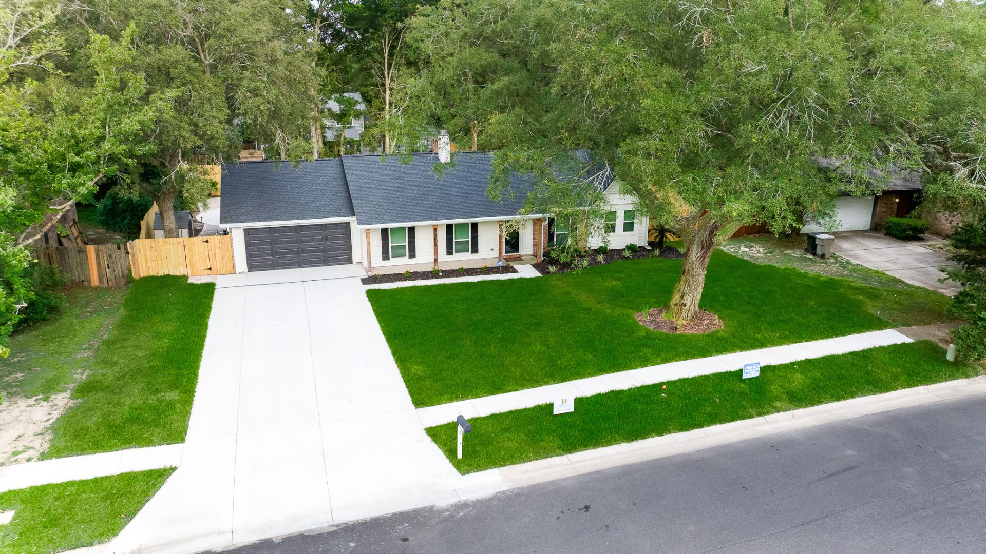 Aerial view of suburban house with green lawn, large tree, and white driveway