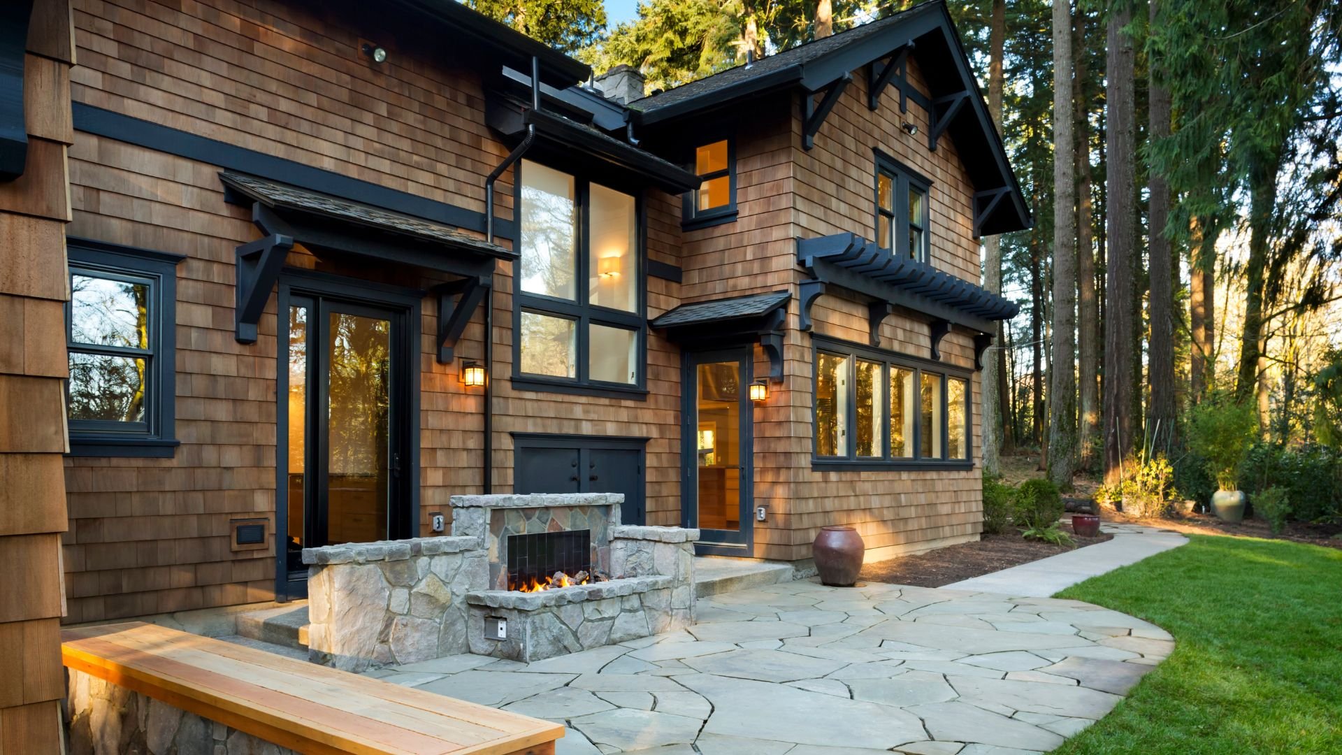 Rustic wood shingle house with stone fireplace and outdoor patio at sunset