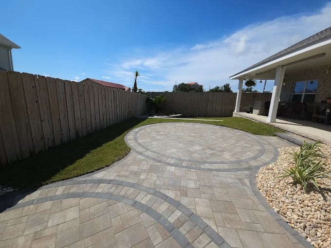 Curved stone patio with landscaped yard and wooden fence on sunny day