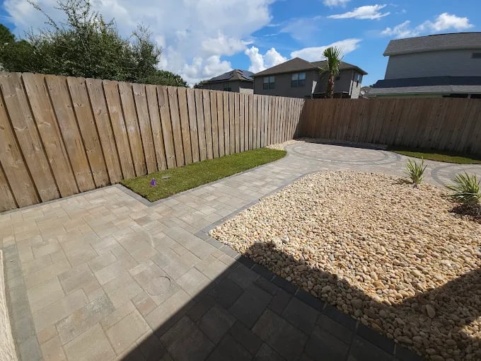 Backyard with stone patio, gravel area, small grass patch, and wooden fence