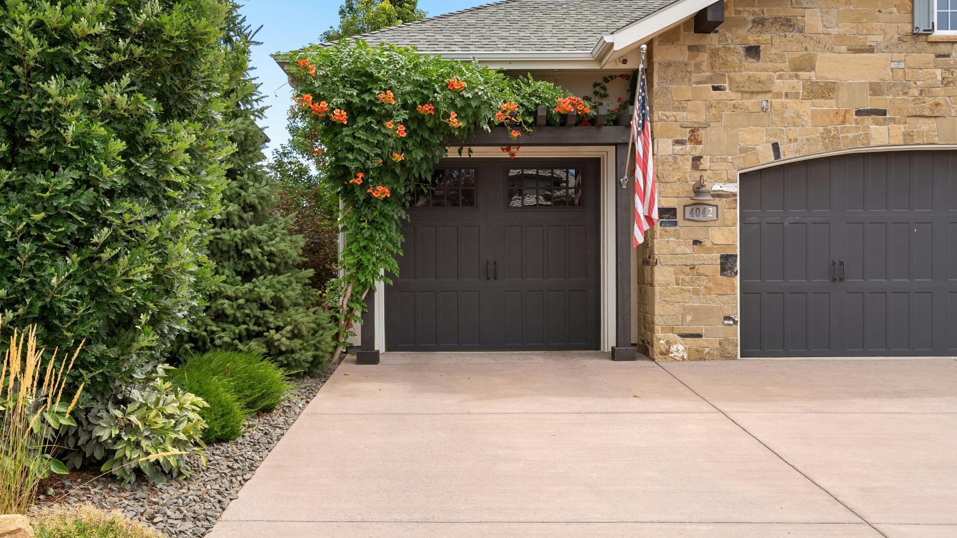 Stone house with dark garage doors, American flag, and orange trumpet vine