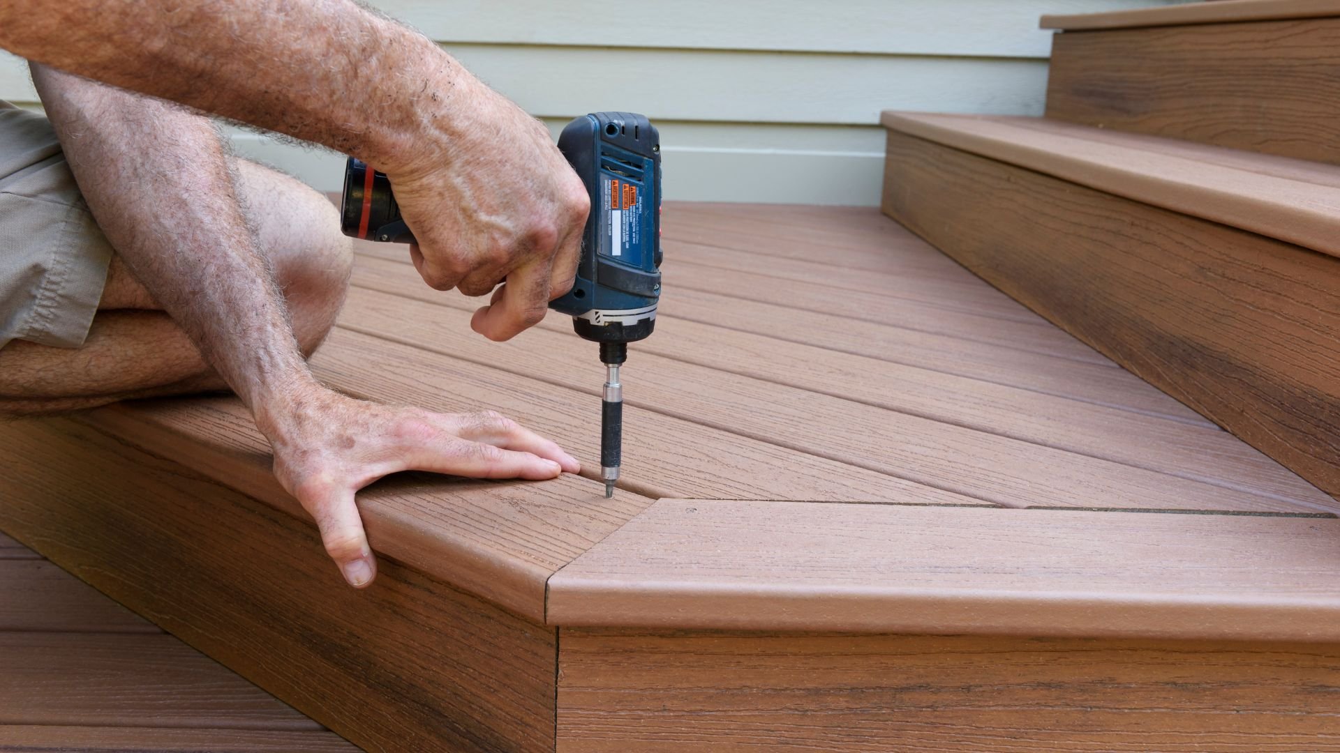 Hand drilling screw into wooden deck or stairs with blue power drill