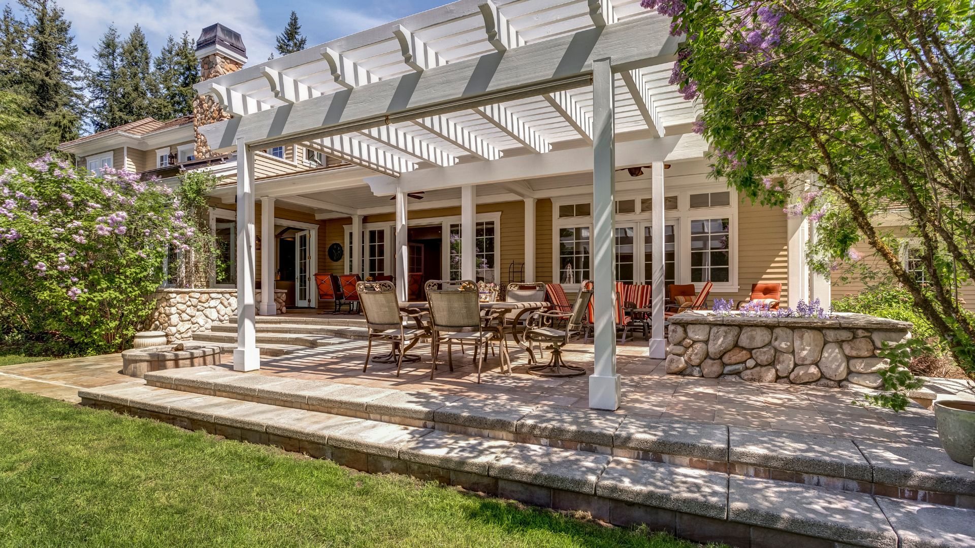 Spacious outdoor patio with white pergola, stone walls, and comfortable seating