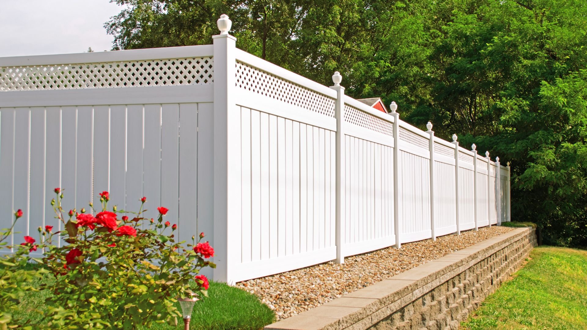 White vinyl fence with red roses on landscaped stone retaining wall